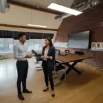 Zak and Sara discussing business inside a UK office lounge in a natural mid‑conversation moment.