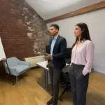 Zak and Sara discussing marketing strategy inside a UK office, mid‑conversation, naturally collaborating.