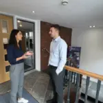 Sara and Adam conversing professionally in a UK office during a collaborative work moment.