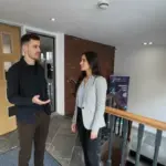 Adam and Sara discussing IT support work inside a UK office, mid‑conversation.